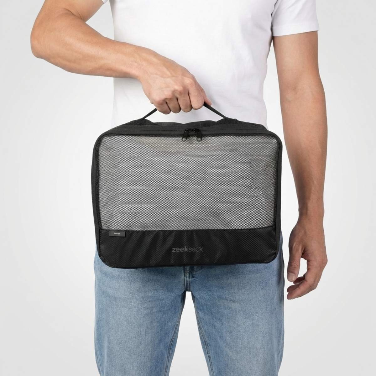 Man i vit t-shirt och jeans håller en stor svart packkub med nätficka på framsidan.