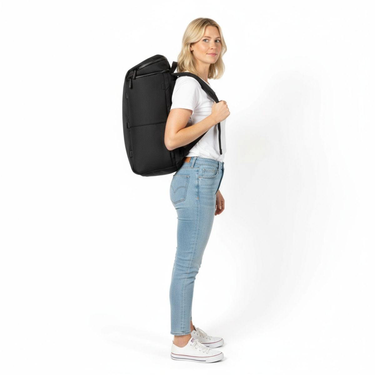 Kvinna i vit t-shirt och jeans bär en svart Zeeksack-ryggsäck, sedd från sidan.