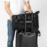 Black backpack attached to the handle of a carry-on suitcase.