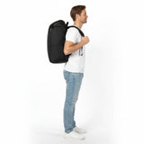 Man in a white T-shirt and jeans wearing a black Zeeksack backpack, viewed from the side.